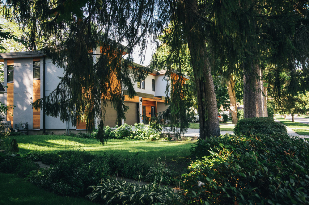 A modoern black, white and light wood coloured house with a palm tree and a driveway that is split into sections with grass details.