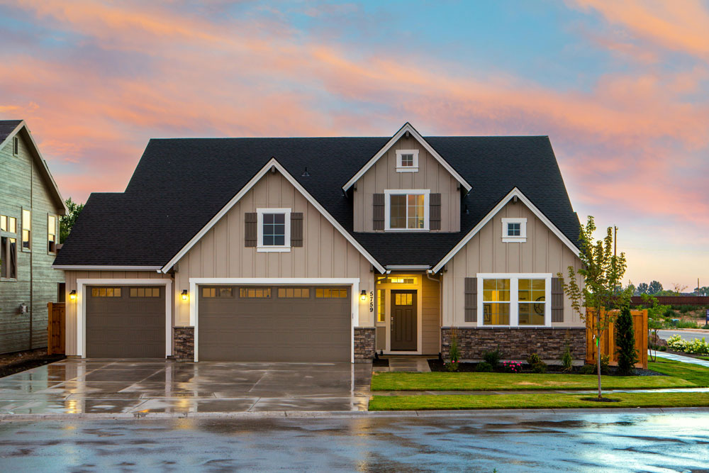 A brown and white house with a small front yard and a driveway with two garage doors.