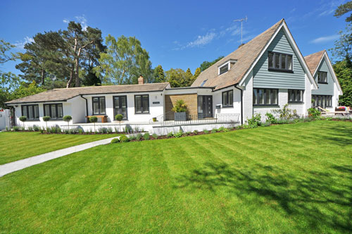A white house with black accents and a brown roof with a walking path and green grass.